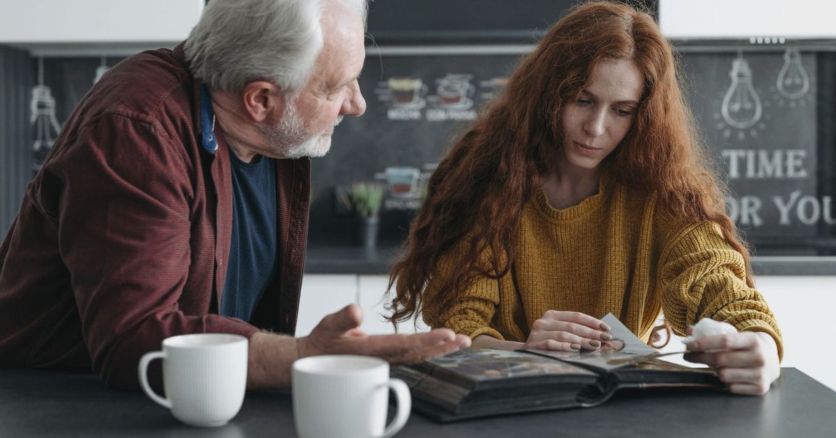 Elderly man and young woman looking at a photo album together, evoking emotions and memories.