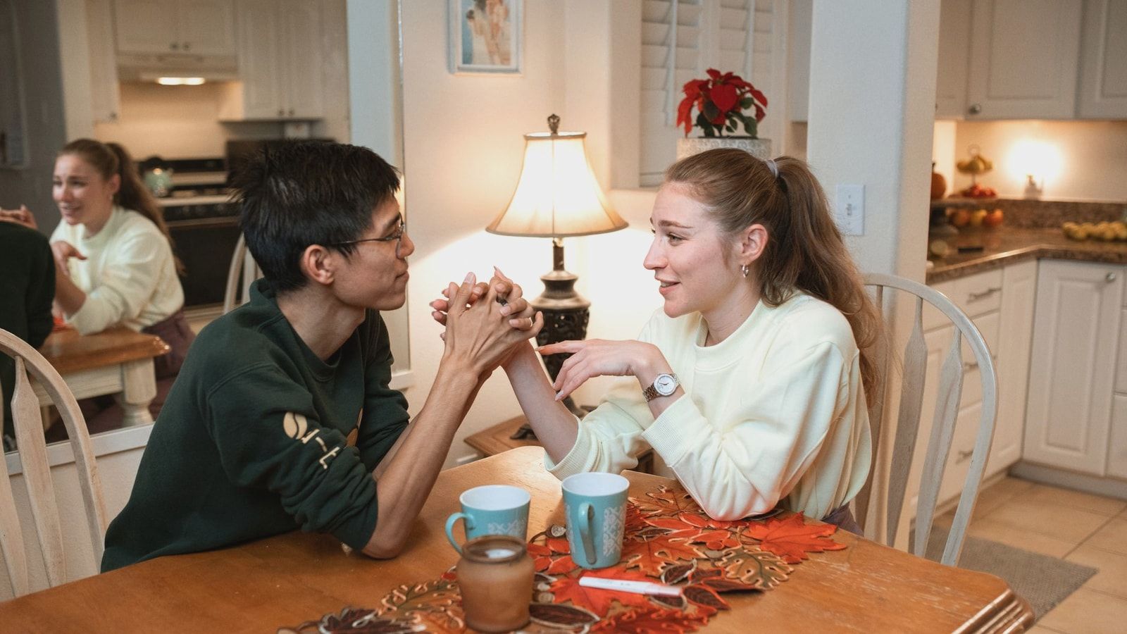 A couple smiling and holding hands at a kitchen table, sharing a warm moment.