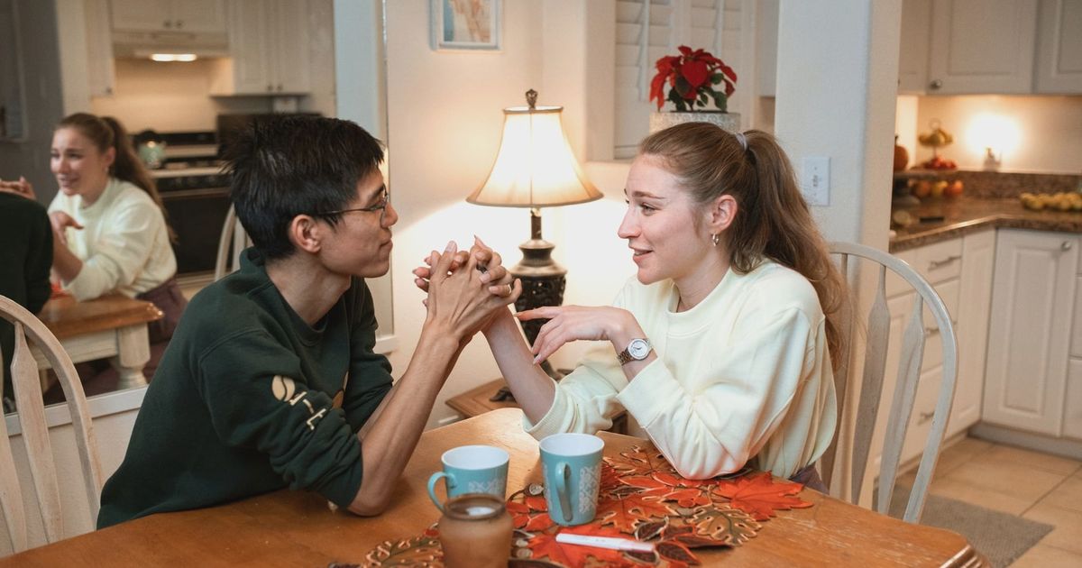 A couple smiling and holding hands at a kitchen table, sharing a warm moment.