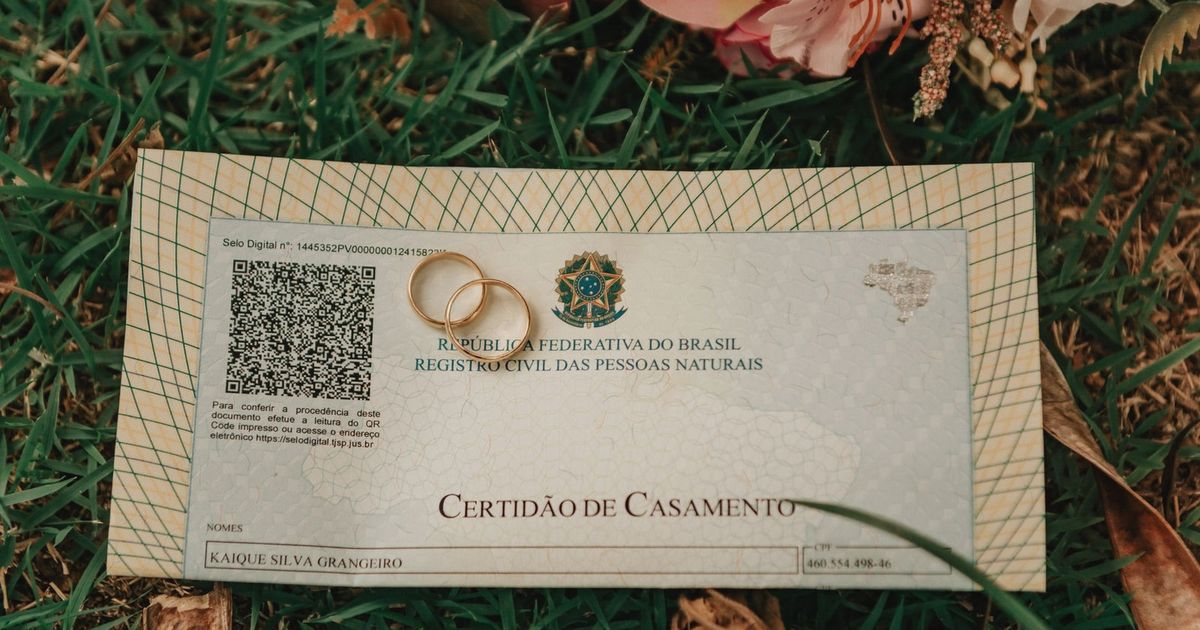 Close-up of a Brazilian marriage certificate with wedding rings and flowers on grass.