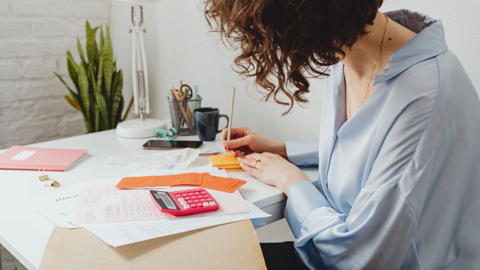 Woman writing with calculator on desk, managing finances indoors.