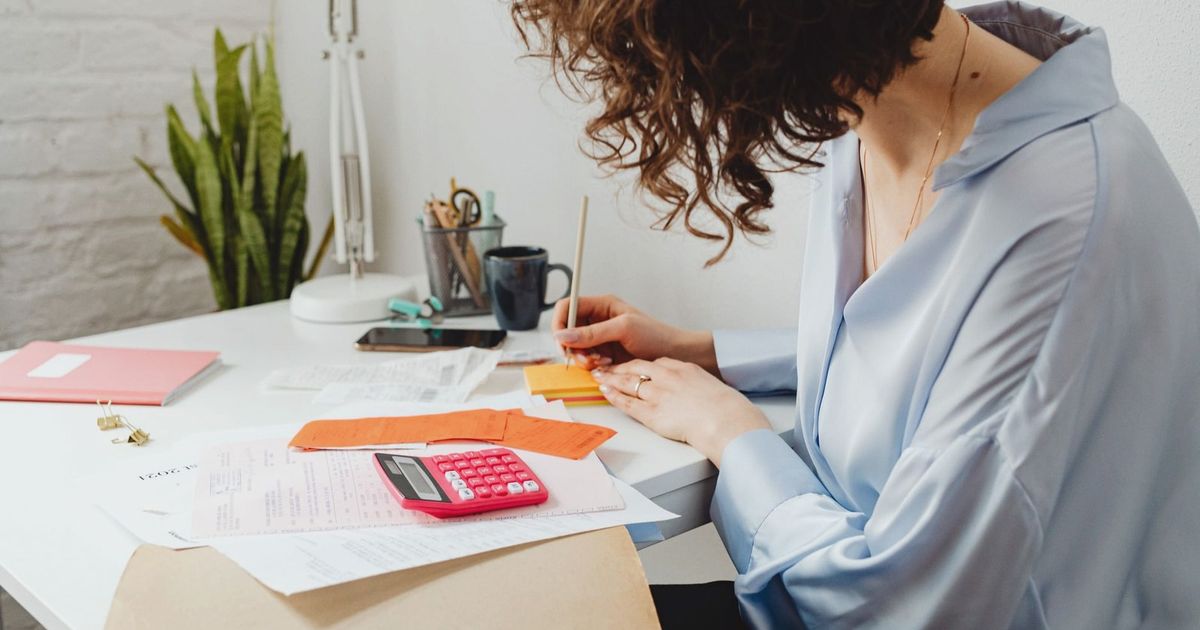 Woman writing with calculator on desk, managing finances indoors.