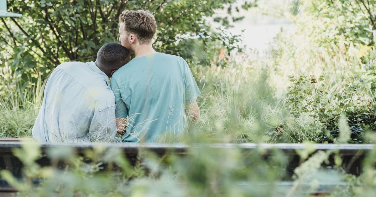Two men sitting together on a bench in a lush park, showcasing affection and companionship.