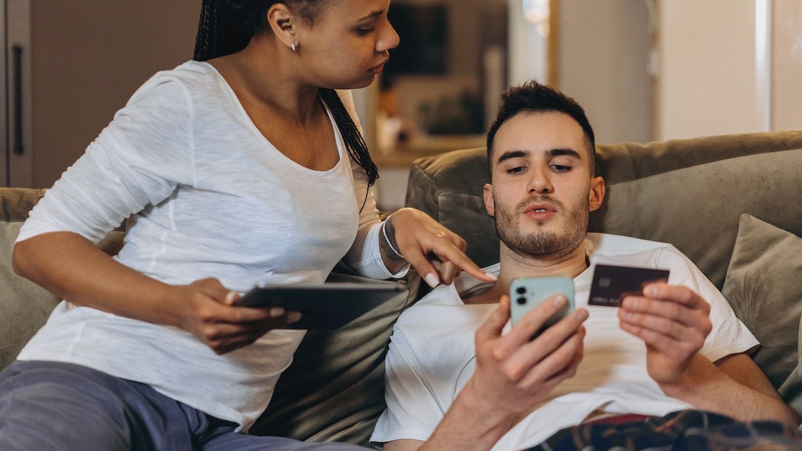 A couple comfortably online shopping at home using a smartphone and tablet for digital purchases.