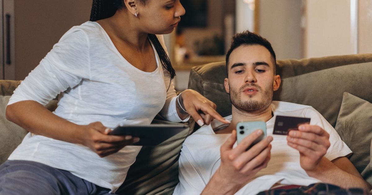 A couple comfortably online shopping at home using a smartphone and tablet for digital purchases.