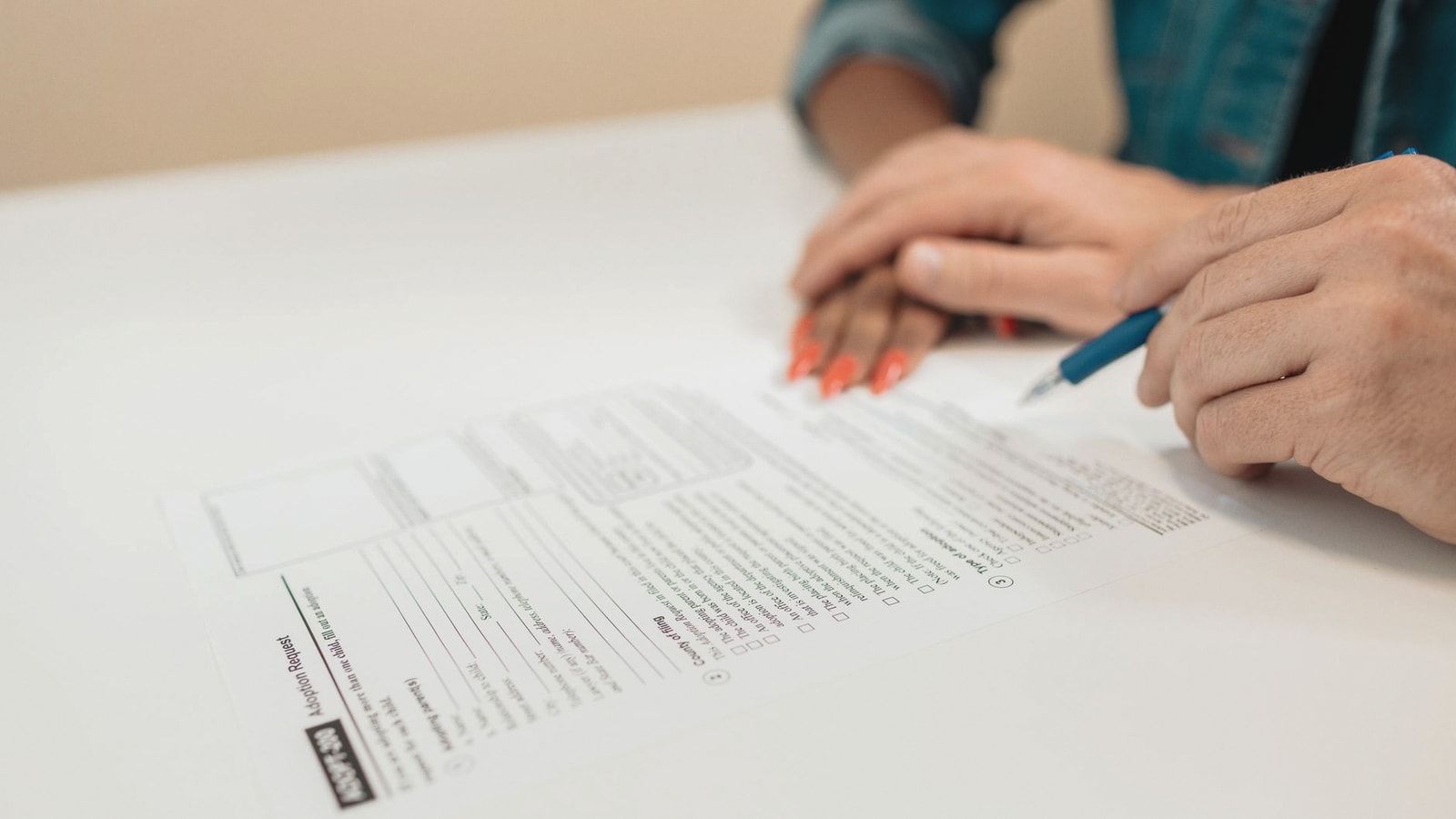 Close-up of hands signing adoption papers in an office environment, symbolizing family and legal process.