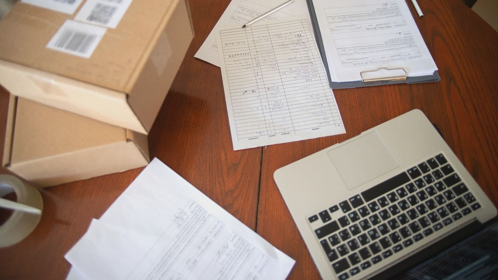 Flat lay of a workspace with laptop, documents, and cardboard boxes for e-commerce operations.