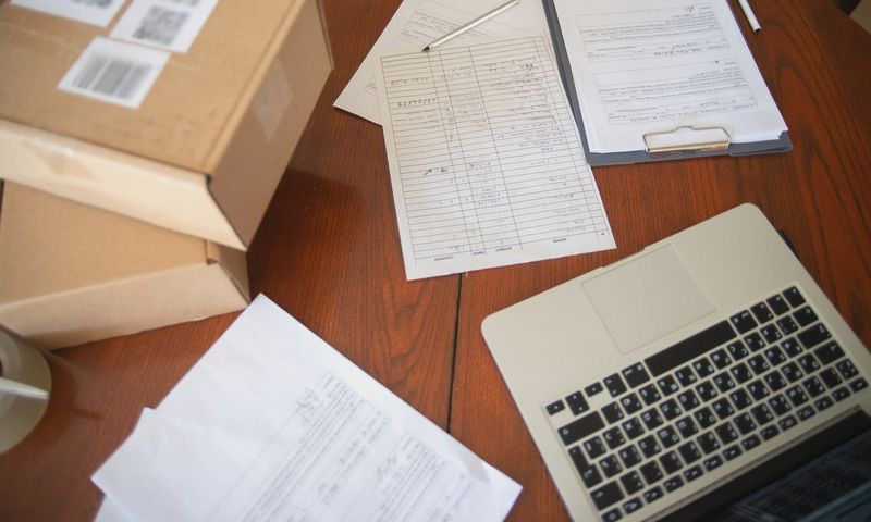 Flat lay of a workspace with laptop, documents, and cardboard boxes for e-commerce operations.