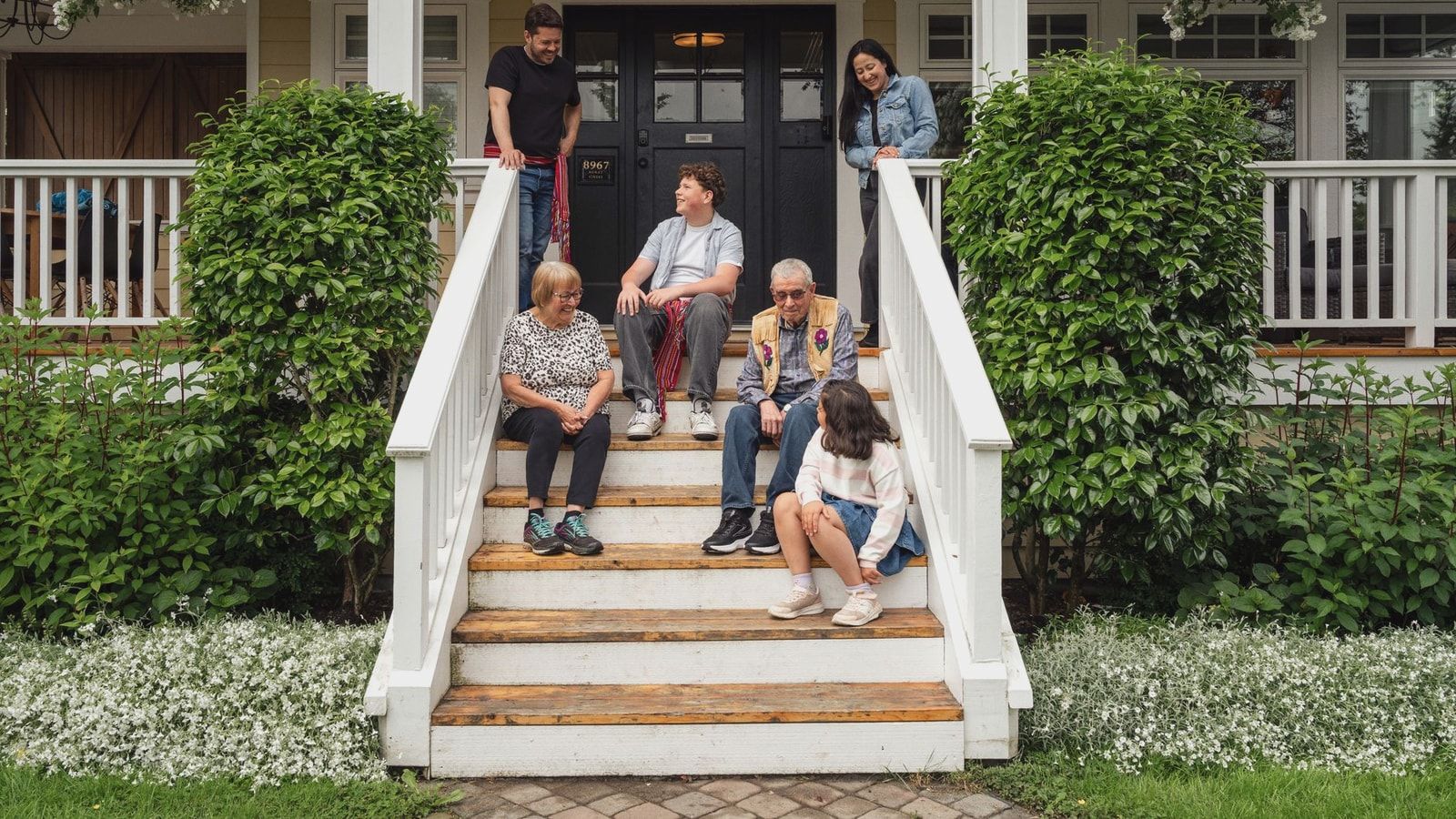 Multigenerational family enjoying a moment on porch steps surrounded by greenery.