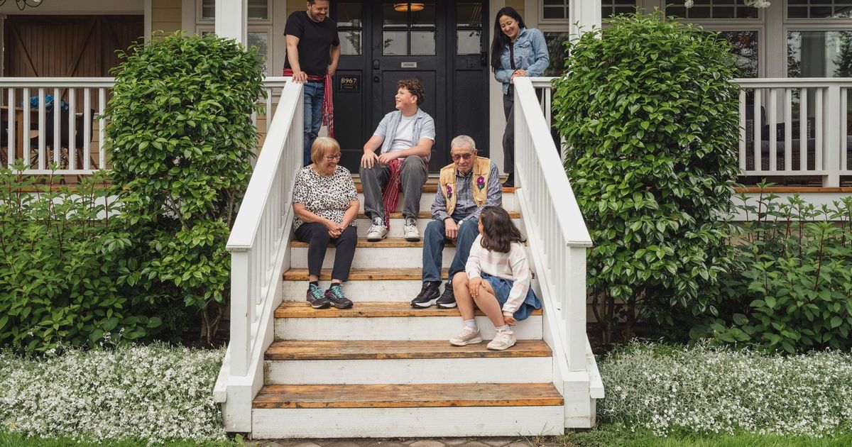 Multigenerational family enjoying a moment on porch steps surrounded by greenery.