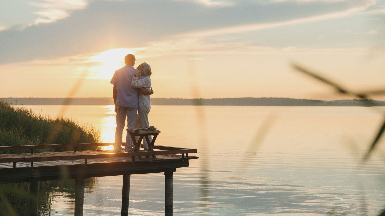 A senior couple embraces on a wooden dock at sunset, exuding tranquility and affection.