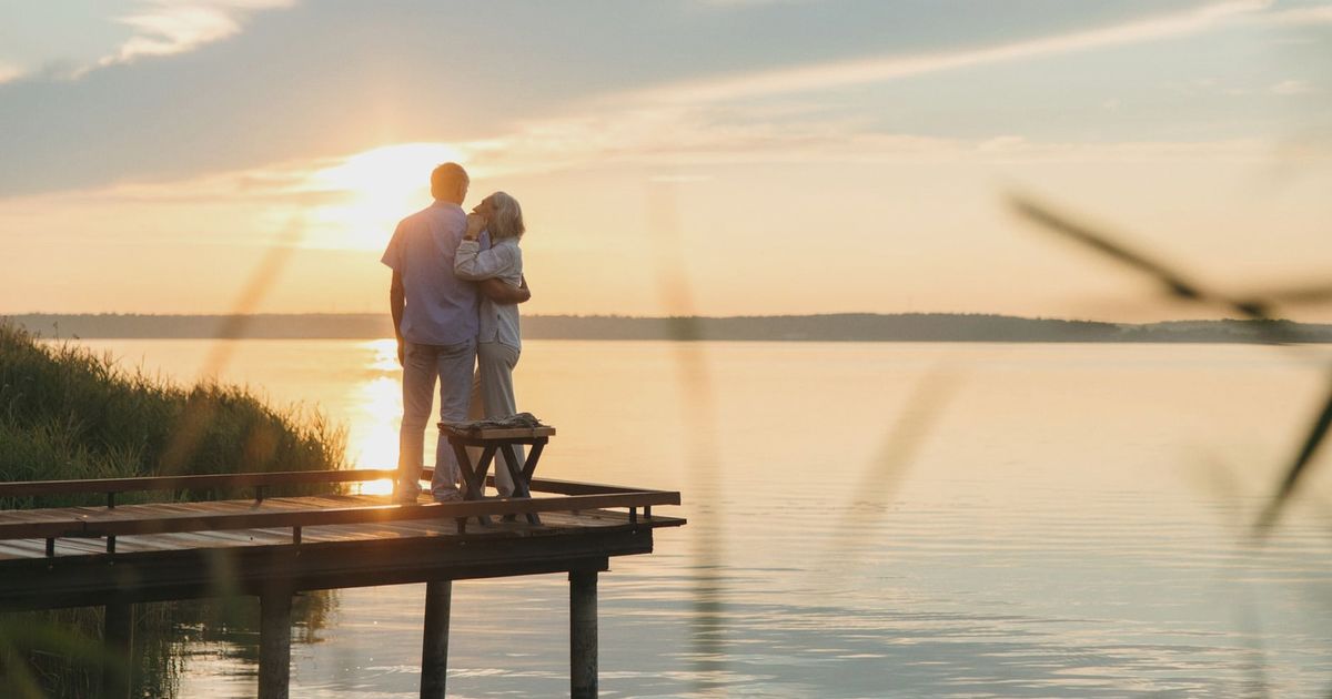 A senior couple embraces on a wooden dock at sunset, exuding tranquility and affection.