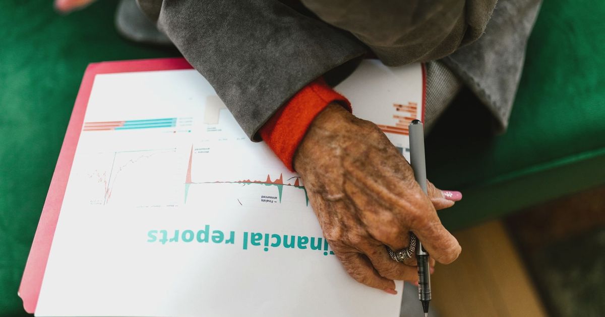 Close-up of an elderly woman holding a pen with a financial report.