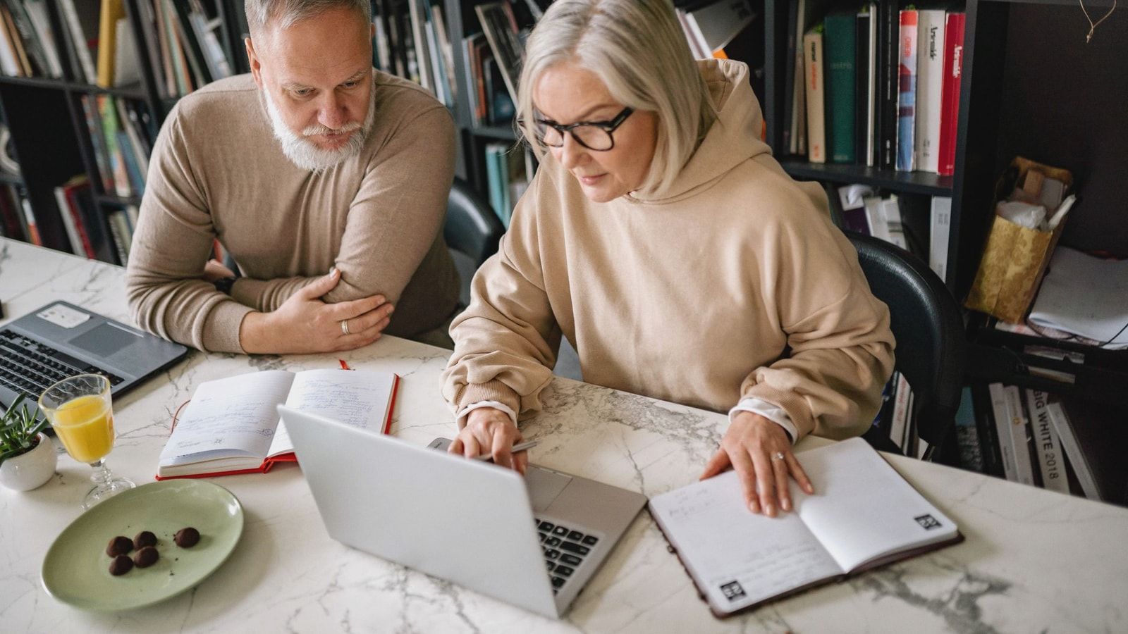 Elderly couple collaborating on laptops in a cozy home office setting.