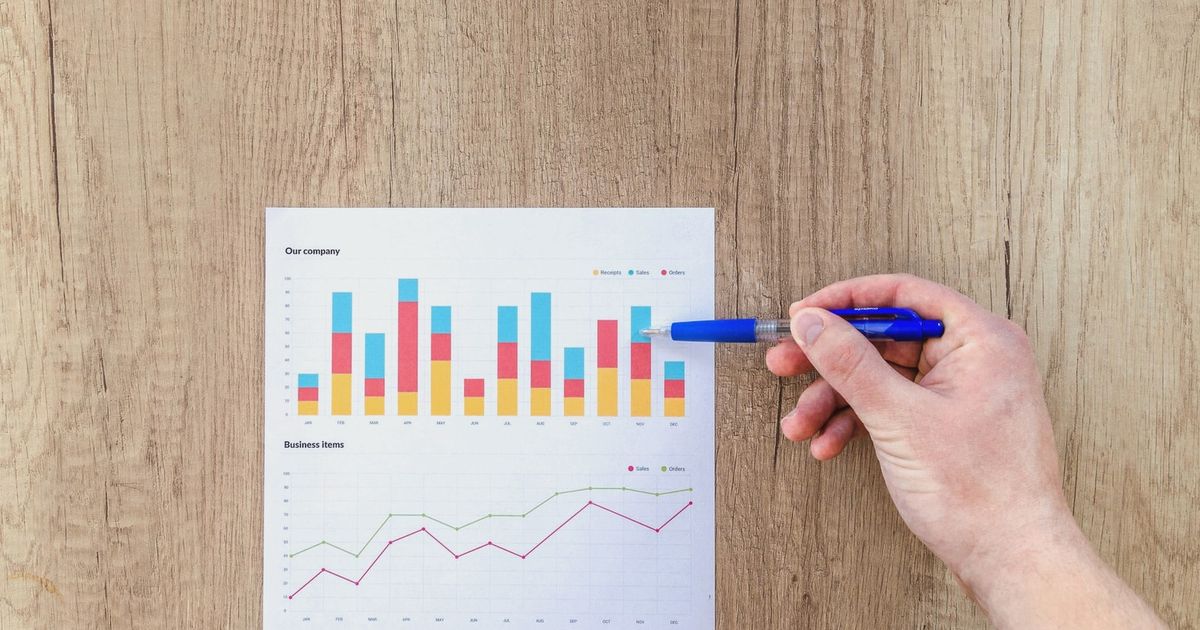 A hand points a pen at business graphs on a wooden table, highlighting data analysis.