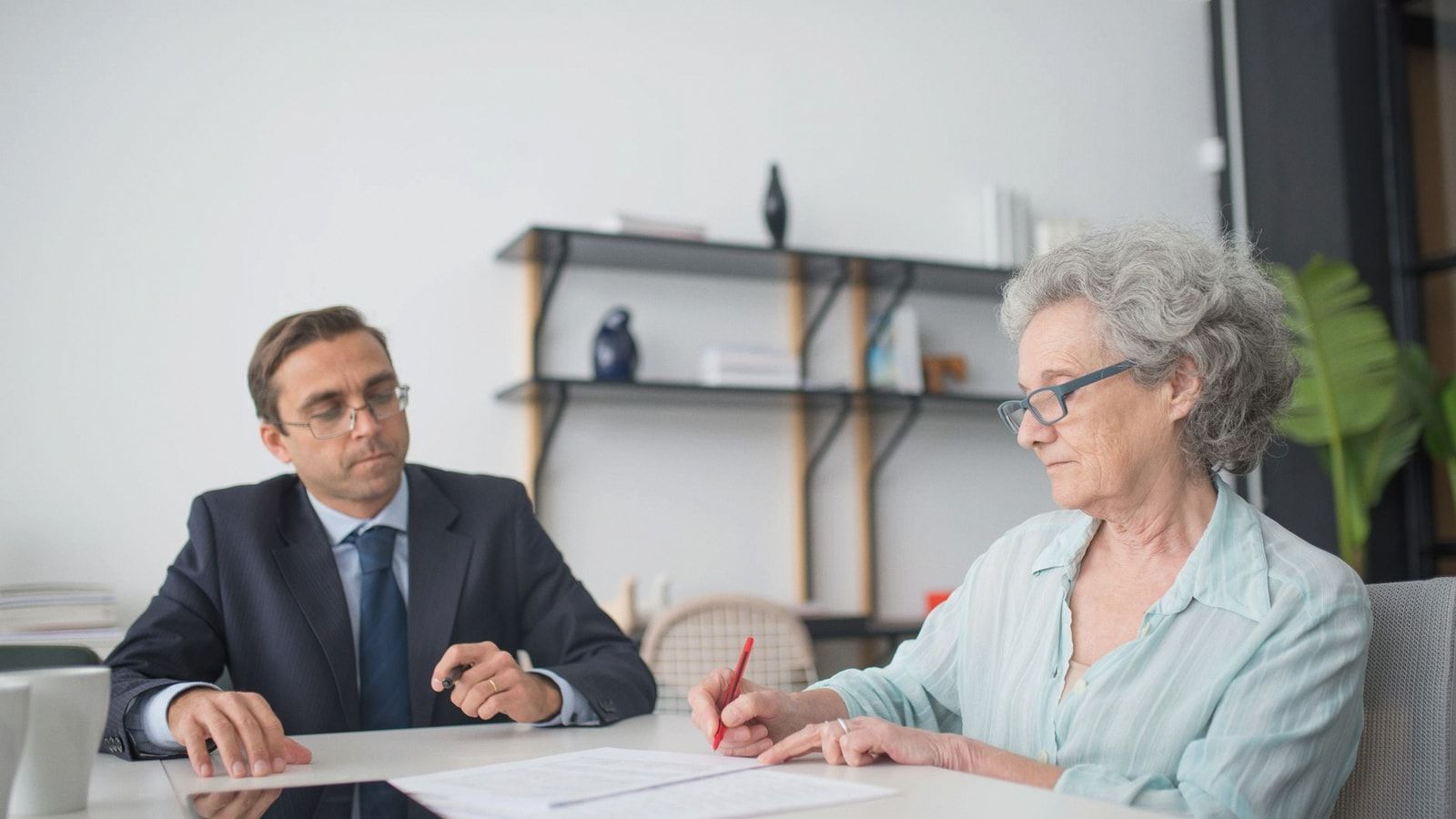 Elderly woman signing paperwork in modern office with consultant.