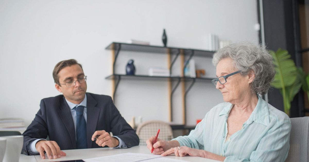 Elderly woman signing paperwork in modern office with consultant.