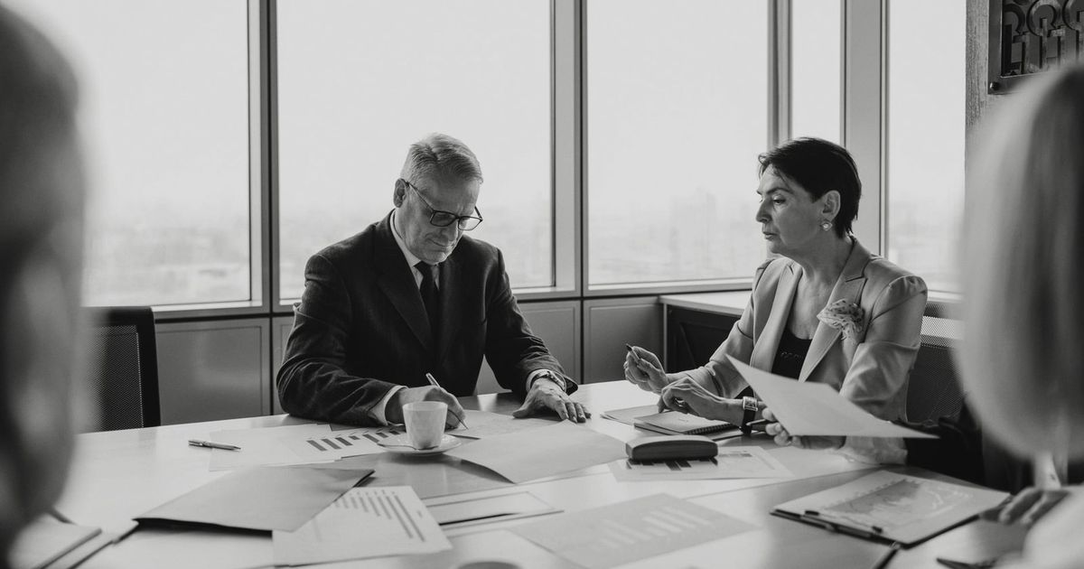 Black and white image of a business meeting with diverse professionals collaborating.
