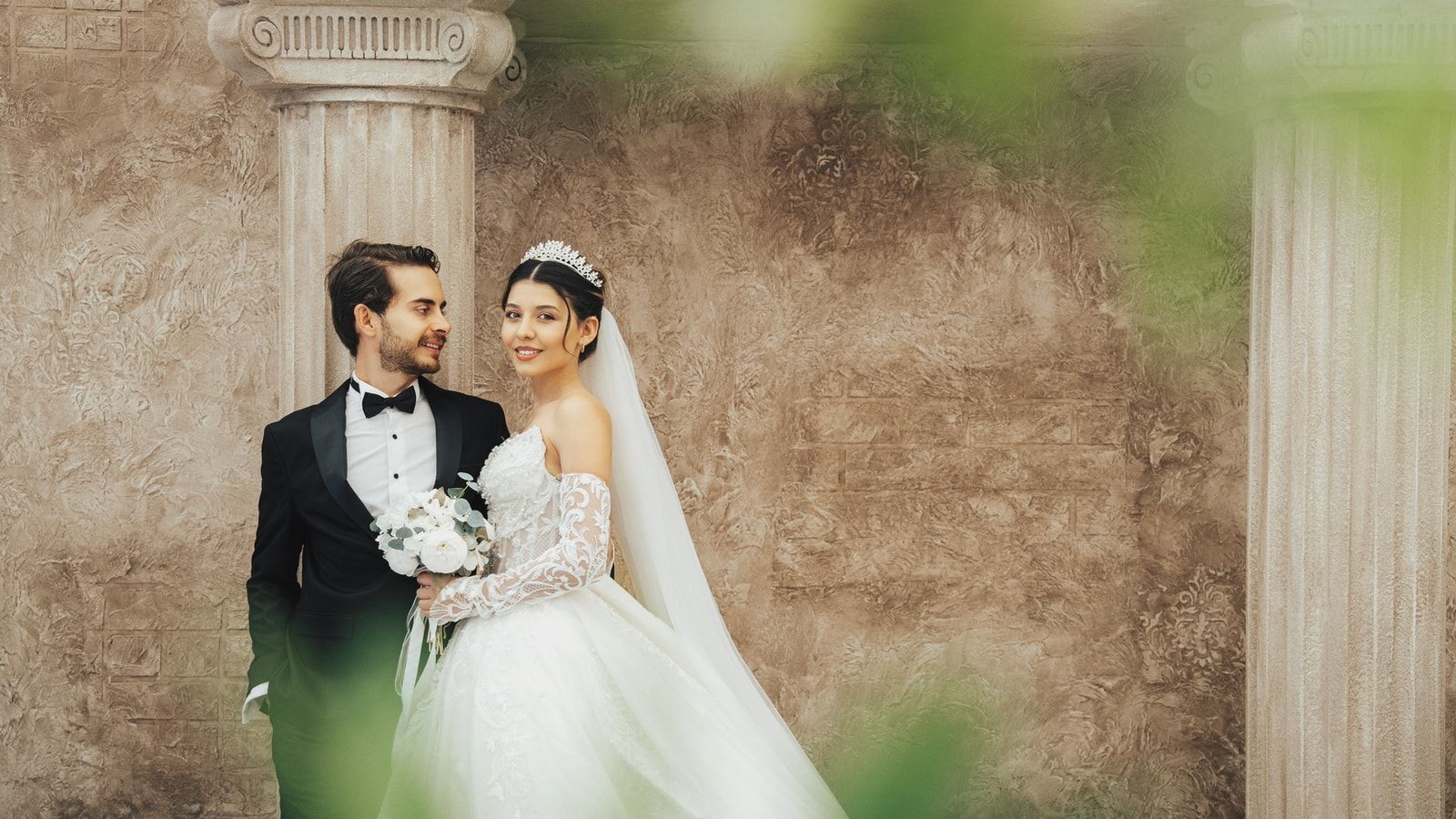 A classic wedding portrait of a couple in elegant attire, set against historic columns in Antalya, Türkiye.