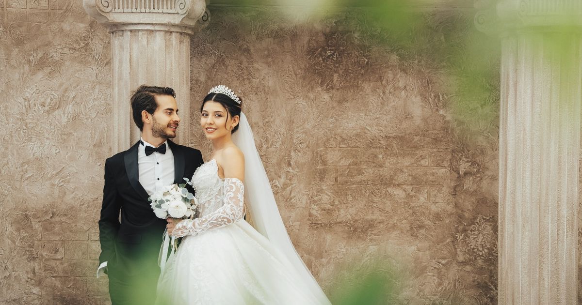 A classic wedding portrait of a couple in elegant attire, set against historic columns in Antalya, Türkiye.