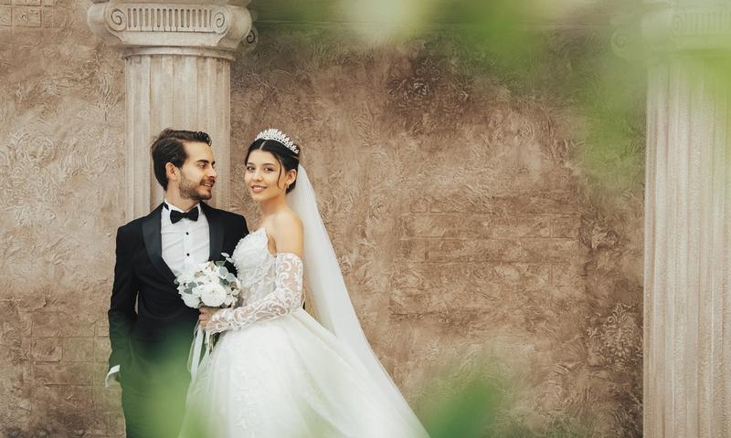 A classic wedding portrait of a couple in elegant attire, set against historic columns in Antalya, Türkiye.