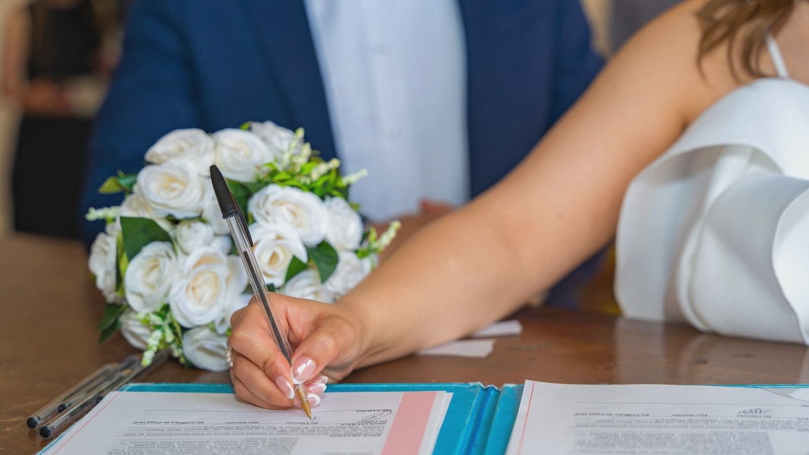 Bride signs marriage certificate during elegant indoor wedding ceremony, symbolizing commitment and togetherness.
