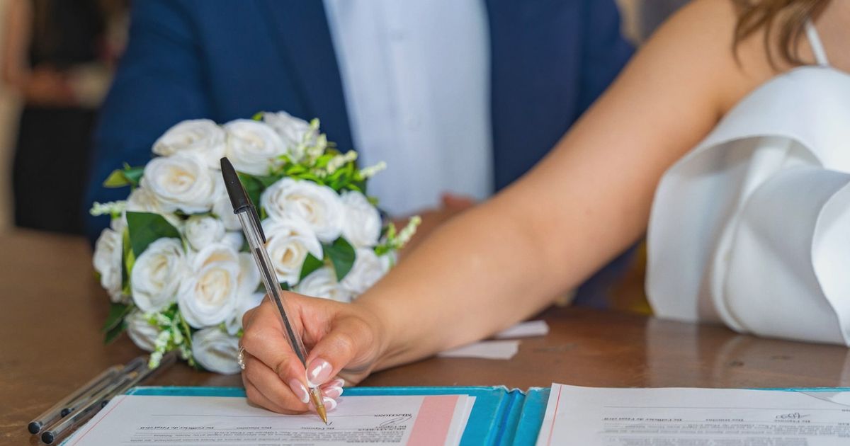 Bride signs marriage certificate during elegant indoor wedding ceremony, symbolizing commitment and togetherness.