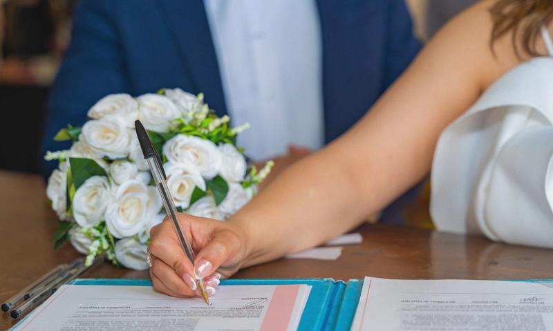Bride signs marriage certificate during elegant indoor wedding ceremony, symbolizing commitment and togetherness.