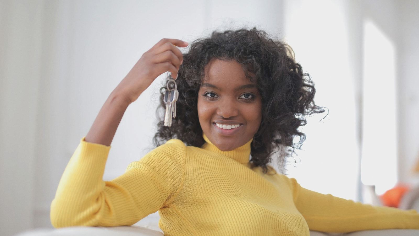 African American woman smiling and holding keys, sitting indoors, symbolizing new home ownership.