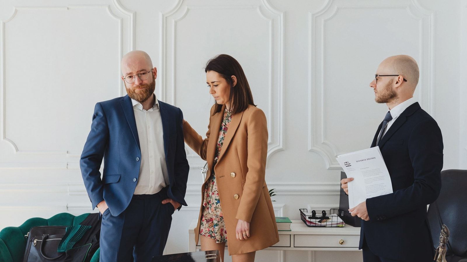 A couple with a lawyer in an office setting, reviewing divorce documents in formal attire.