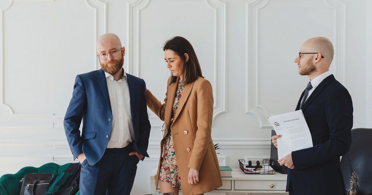 A couple with a lawyer in an office setting, reviewing divorce documents in formal attire.