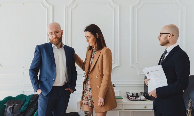 A couple with a lawyer in an office setting, reviewing divorce documents in formal attire.