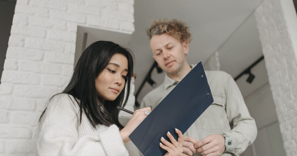 Asian woman signing for package delivery indoors, interacting with courier.