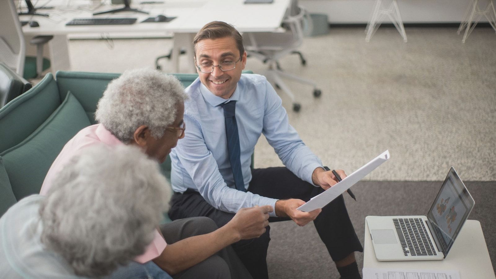 Consultant discussing financial plans with senior clients in a modern office setting, using documents and a laptop.