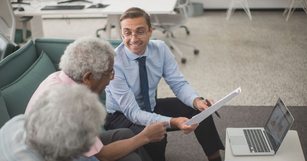 Consultant discussing financial plans with senior clients in a modern office setting, using documents and a laptop.