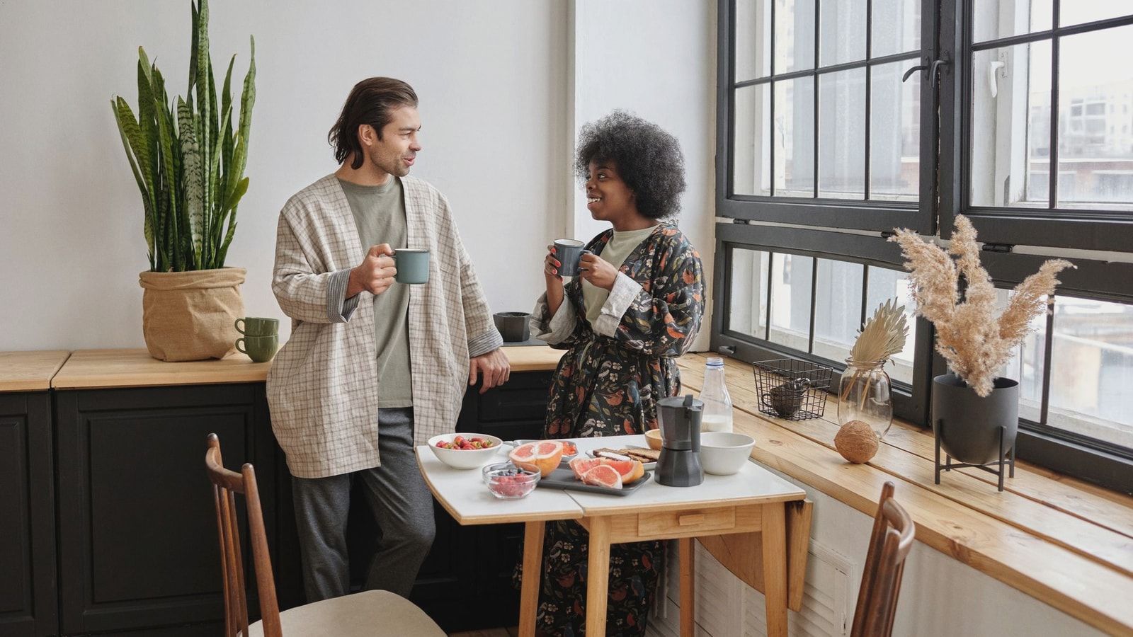 A joyful couple enjoys a morning coffee and healthy breakfast of grapefruit in their cozy apartment.
