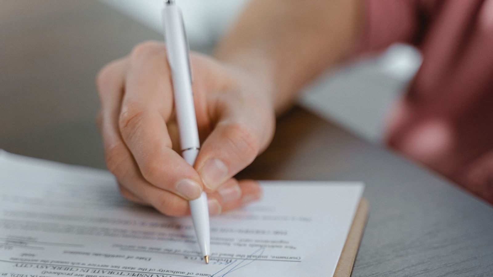 Detailed view of a hand writing a signature on an official document with a ballpoint pen.