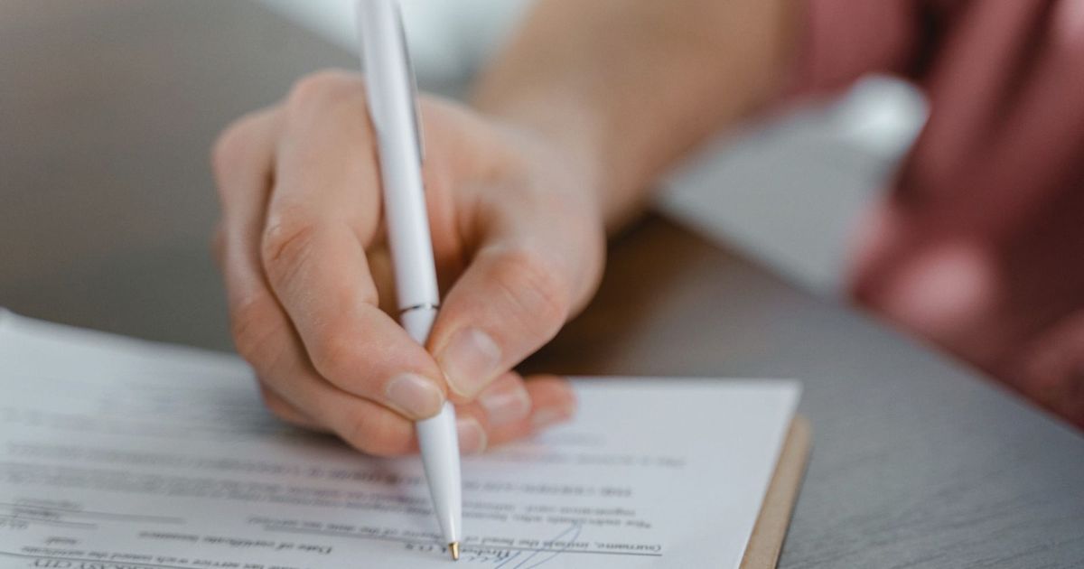 Detailed view of a hand writing a signature on an official document with a ballpoint pen.