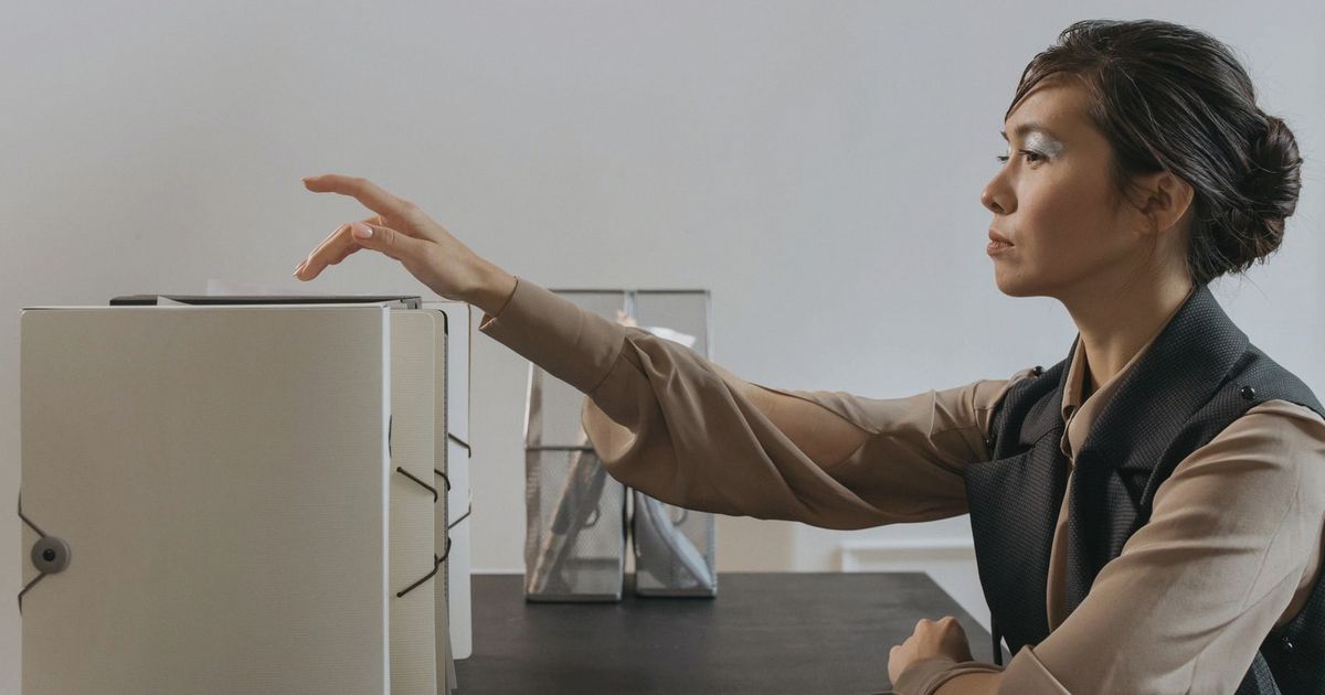 Asian woman efficiently organizing documents at an office desk.