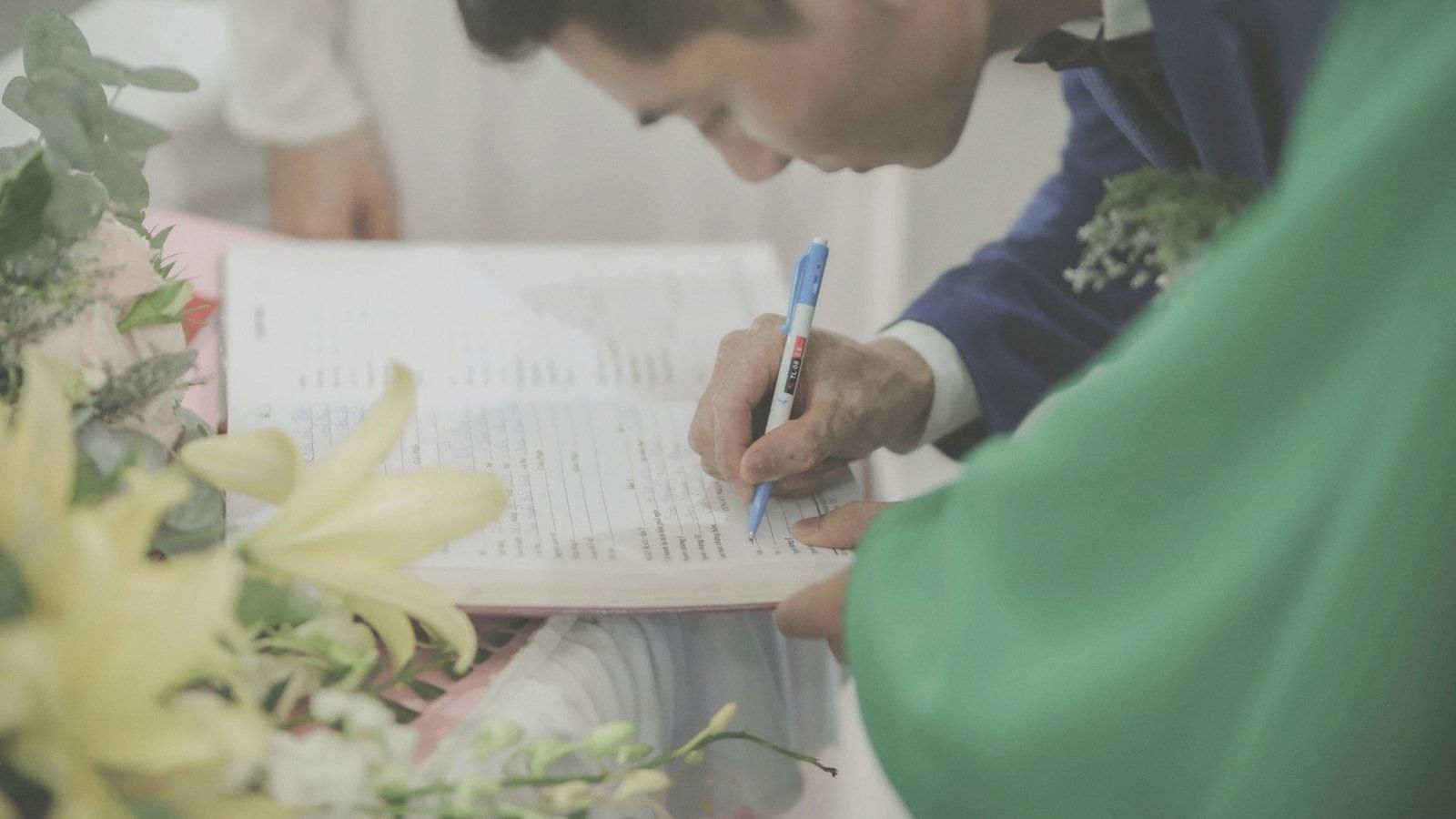 A man in formal attire signs a marriage document during a wedding celebration.
