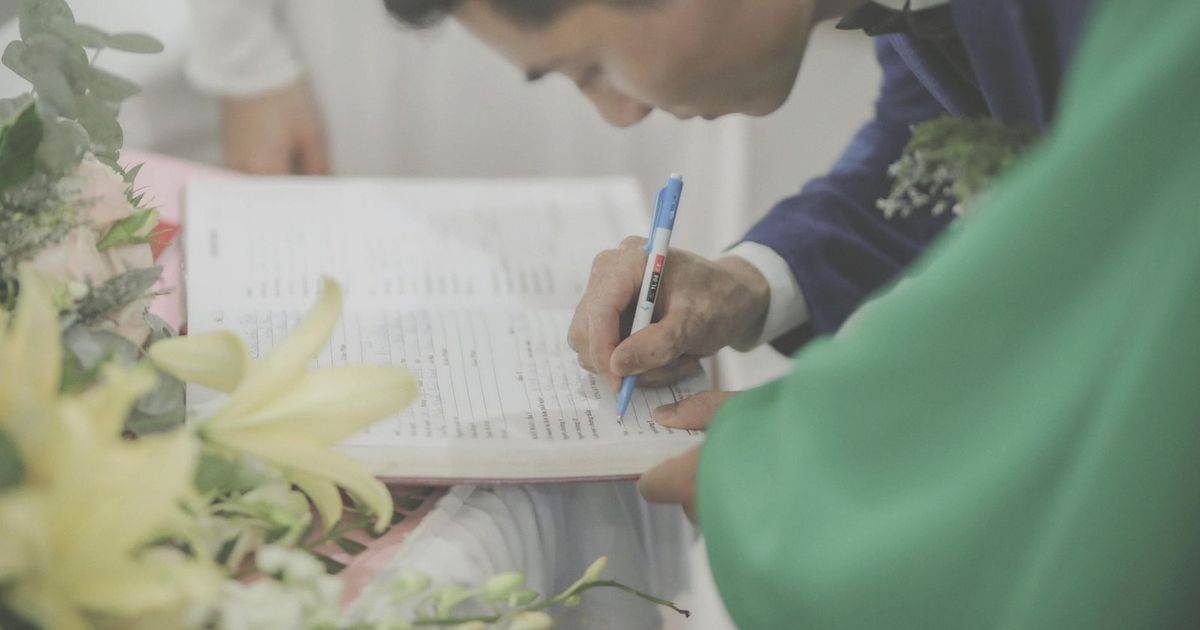 A man in formal attire signs a marriage document during a wedding celebration.