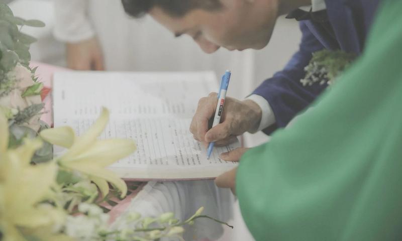 A man in formal attire signs a marriage document during a wedding celebration.
