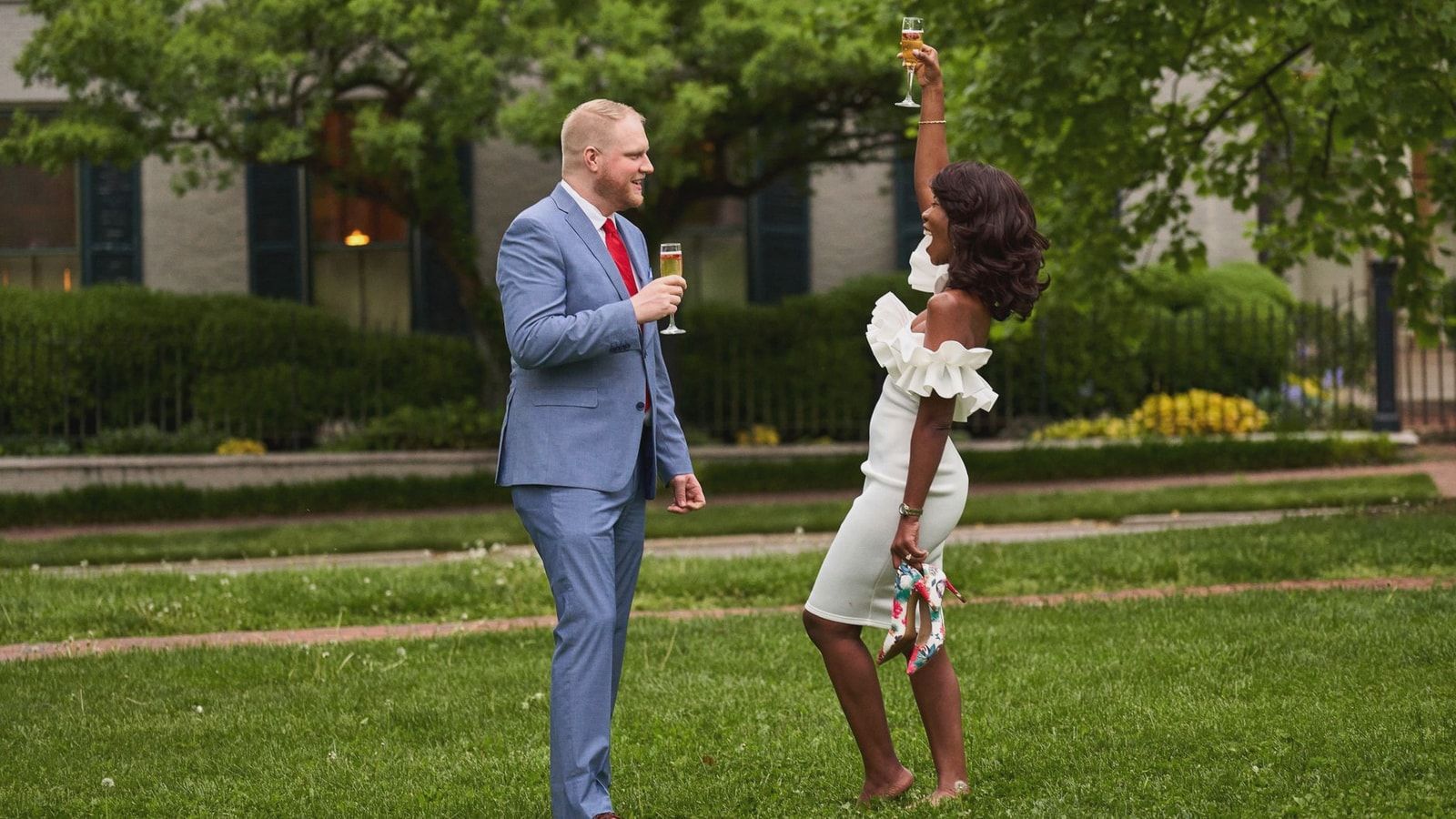 Couple celebrating their engagement with a champagne toast in a garden setting.