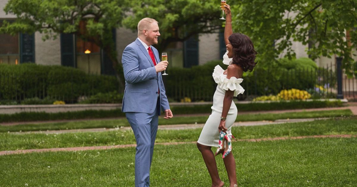 Couple celebrating their engagement with a champagne toast in a garden setting.