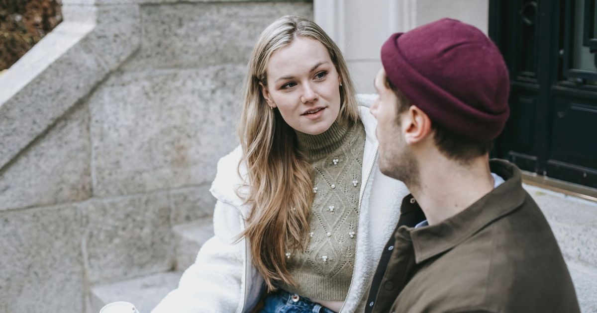 Man and woman talking sitting on steps outside house and having hot beverage in paper cups