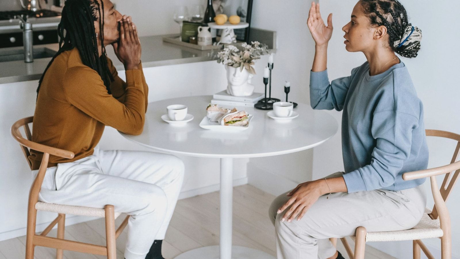 Side view of young African American female sitting at table while arguing with male in casual clothes