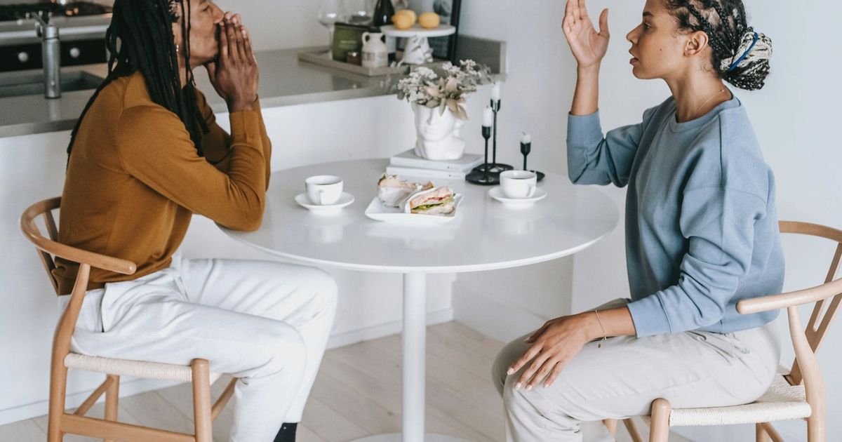 Side view of young African American female sitting at table while arguing with male in casual clothes