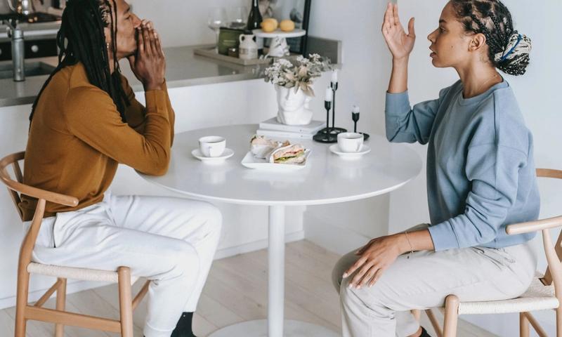 Side view of young African American female sitting at table while arguing with male in casual clothes