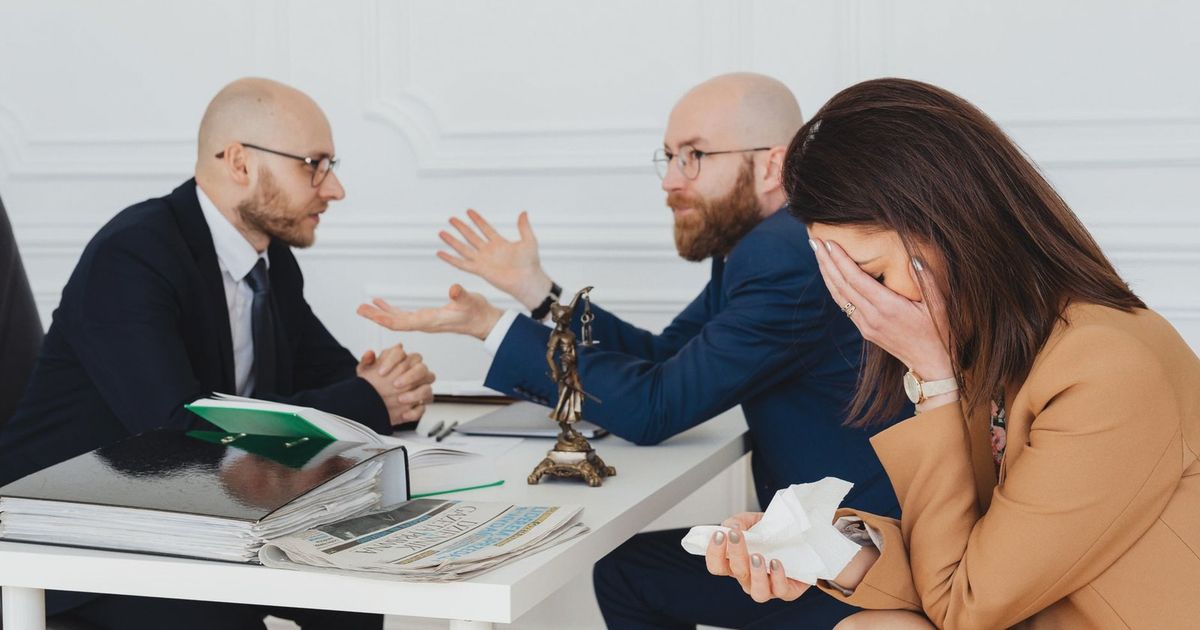 A lawyer mediates an emotional settlement discussion with a distressed couple in a legal office.