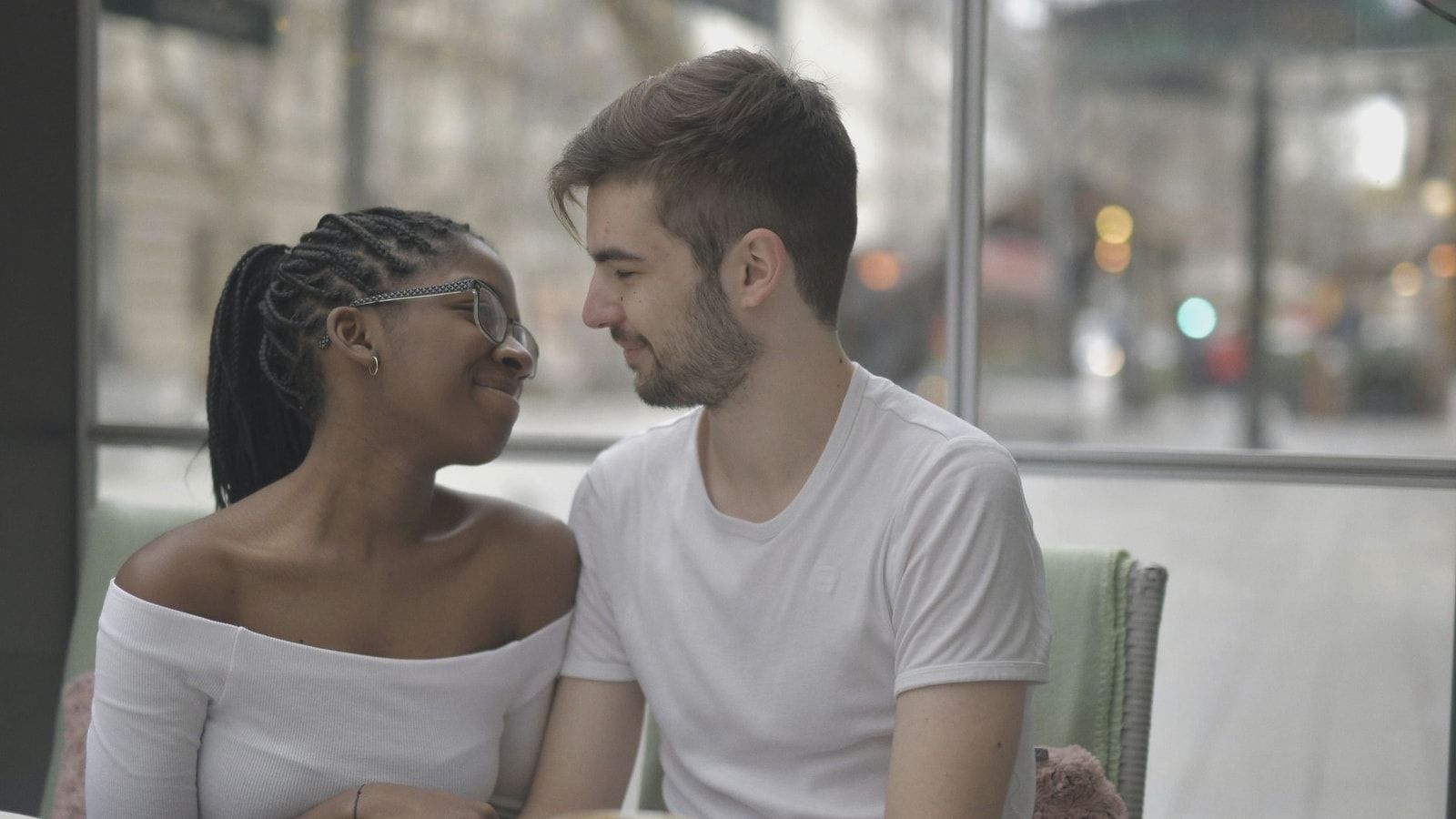 A loving multiracial couple shares a joyful moment over coffee, embracing affection and diversity indoors.
